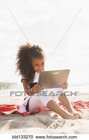 Mixed race girl using digital tablet on beach View Large Photo Image Stock Image - Mixed race girl using digital tablet on beach. Fotosearch