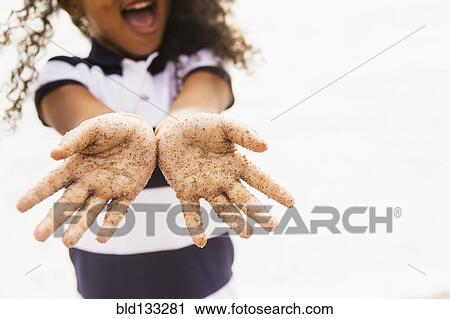 Stock Image - Mixed race girl with sandy hands on beach. Fotosearch