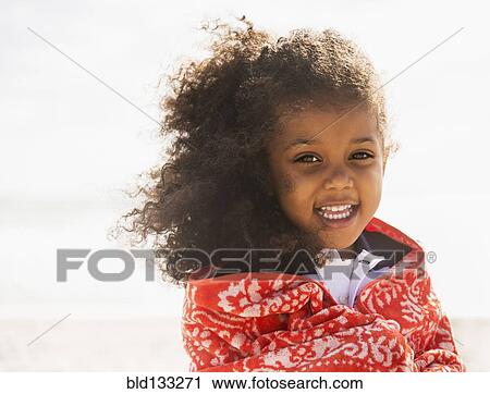 Stock Image - Mixed race girl wrapped in towel on beach. Fotosearch
