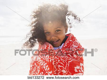 Stock Image - Mixed race girl wrapped in towel on beach. Fotosearch