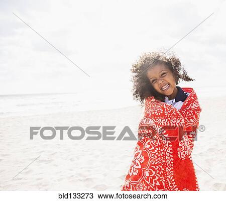 Stock Image - Mixed race girl wrapped in towel on beach. Fotosearch