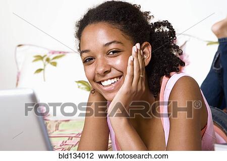 Mixed race teenage girl using laptop on bed View Large Photo Image Stock Image - Mixed race teenage girl using laptop on bed. Fotosearch