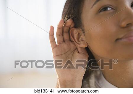 Stock Image - Mixed race woman cupping her ear. Fotosearch