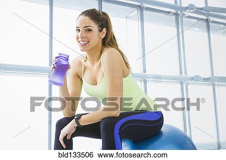 Stock Photograph - Mixed race woman drinking water in gym. Fotosearch