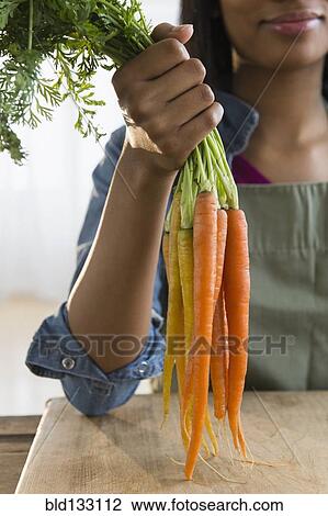 Mixed race woman holding bunch of carrots View Large Photo Image Stock Image - Mixed race woman holding bunch of carrots. Fotosearch