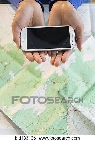 Stock Photography - Mixed race woman holding cell phone over map. Fotosearch