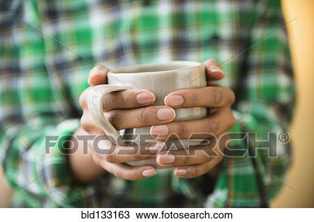 Stock Image - Mixed race woman holding cup of coffee. Fotosearch