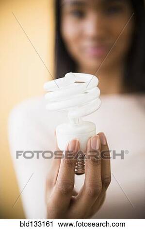 Stock Image - Mixed race woman holding light bulb. Fotosearch