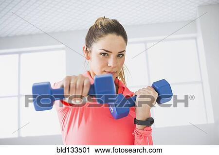 Stock Image - Mixed race woman lifting weights in gym. Fotosearch