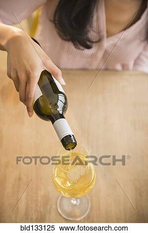 Stock Photography - Mixed race woman pouring glass of wine. Fotosearch