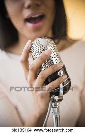 Picture - Mixed race woman singing into vintage microphone. Fotosearch