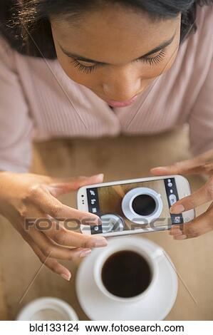 Mixed race woman taking cell phone picture of coffee cup View Large Photo Image Picture - Mixed race woman taking cell phone picture of coffee cup. Fotosearch