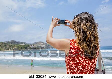 Picture - Mixed race woman taking pictures of tropical beach. Fotosearch
