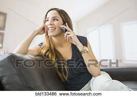 Stock Photograph - Mixed race woman talking on cell phone on sofa. Fotosearch