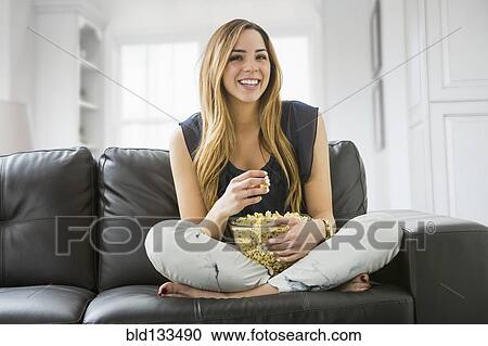 Stock Image - Mixed race woman watching television on sofa. Fotosearch