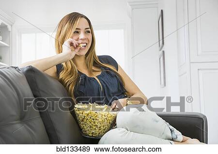 Stock Photo - Mixed race woman watching television on sofa. Fotosearch