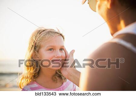Stock Image - Mother cupping daughter's face on beach. Fotosearch
