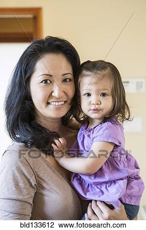 Stock Image - Mother holding daughter in kitchen. Fotosearch