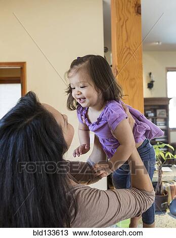 Stock Image - Mother holding daughter in kitchen. Fotosearch