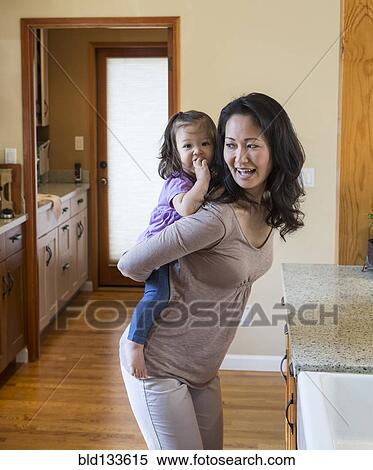 Stock Photography - Mother holding daughter in kitchen. Fotosearch