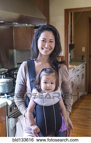Stock Photograph - Mother holding daughter in sling in kitchen. Fotosearch