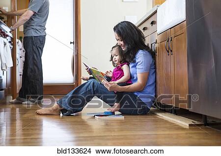 Picture - Mother reading to daughter in kitchen. Fotosearch