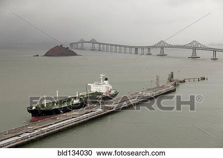 Stock Image - Oil tanker offloading in urban dock. Fotosearch