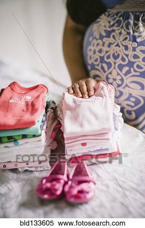 Stock Photography - Pregnant Asian woman folding baby clothes. Fotosearch