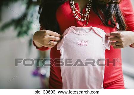 Stock Image - Pregnant Asian woman holding baby clothes. Fotosearch