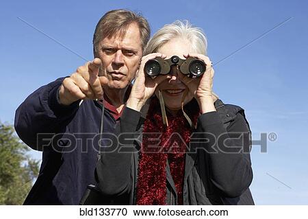 Stock Image - Senior Caucasian couple using binoculars outdoors. Fotosearch