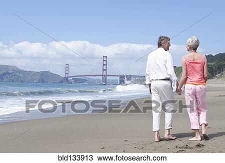 Stock Image - Senior Caucasian couple walking by Golden Gate Bridge, San Francisco, California, United States. Fotosearch