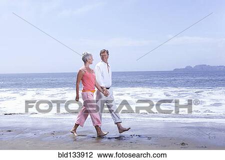 Stock Image - Senior Caucasian couple walking on beach. Fotosearch
