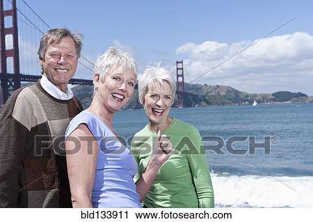Stock Image - Senior Caucasian friends smiling by Golden Gate Bridge, San Francisco, California, United States. Fotosearch
