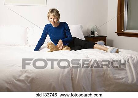 Stock Photograph - Senior Caucasian woman petting cat on bed. Fotosearch