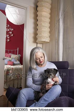 Stock Photography - Senior Caucasian woman petting dog in armchair. Fotosearch