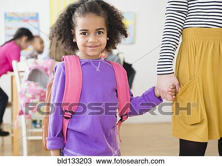 Stock Image - Student and teacher holding hands in classroom. Fotosearch