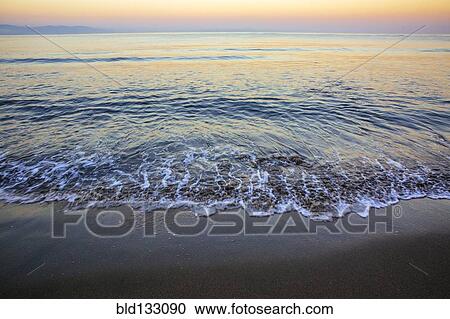 Stock Image - Waves washing up on sandy beach. Fotosearch