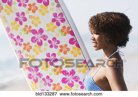Stock Photo - Woman carrying surfboard on beach. Fotosearch