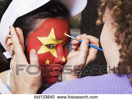Stock Image - Woman painting Chinese flag on Chinese girl's face. Fotosearch