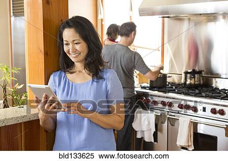 Stock Photography - Woman using digital tablet in kitchen. Fotosearch