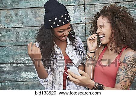 Stock Image - Women listening to mp3 player on city street. Fotosearch