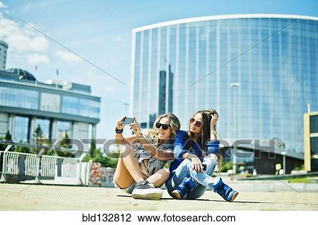 Stock Image - Women taking picture on city street. Fotosearch