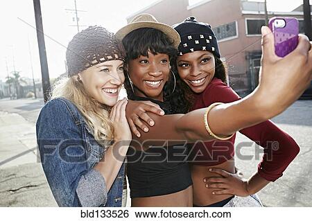 Stock Photograph - Women taking pictures together on city street. Fotosearch