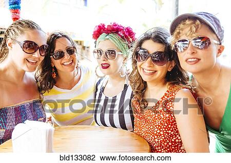Stock Image - Women wearing sunglasses together at cafe. Fotosearch