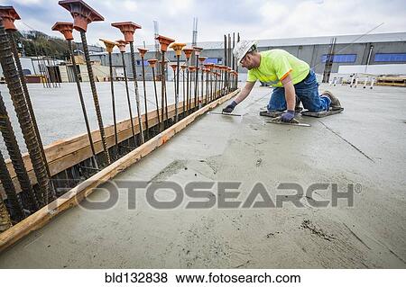 Stock Photo - Worker finishing concrete at construction site. Fotosearch