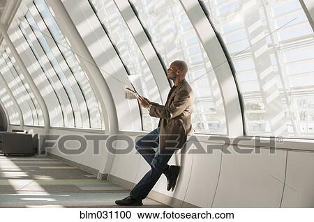 Stock Image - African American businessman reading newspaper in lobby. Fotosearch