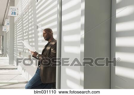 Stock Image - African American businessman reading papers in office. Fotosearch