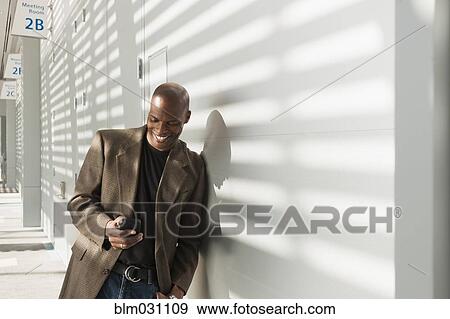 Stock Photo - African American businessman using cell phone in office. Fotosearch