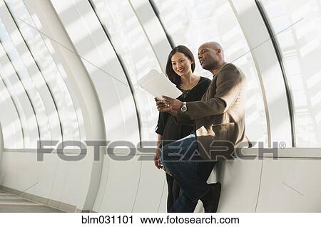 Stock Image - Business people reading paperwork in lobby. Fotosearch