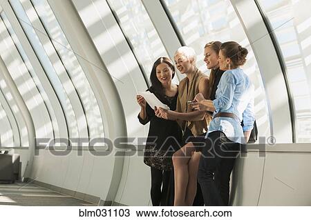 Stock Image - Businesswomen reading paperwork in lobby. Fotosearch